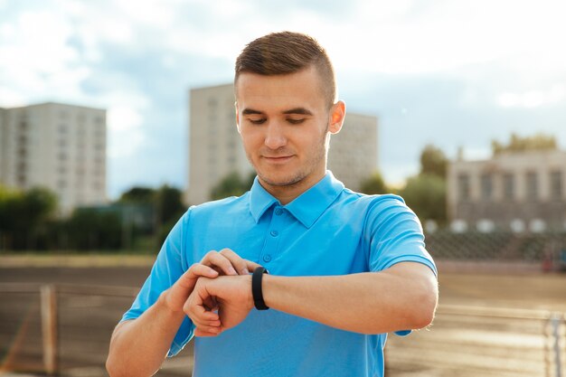 Deportista, guapo mirando y mirando su reloj después de correr al aire libre