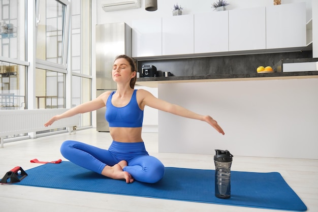 Foto gratuita deportista levantando las manos y respirando inhalando aire sentada en una alfombra de yoga meditando haciendo yoga