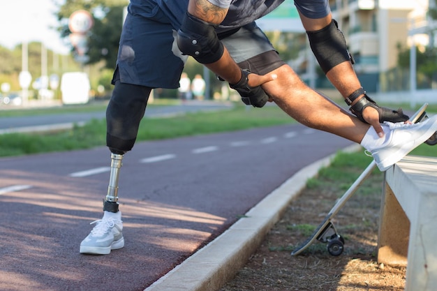 Deportista con pierna mecánica preparándose para entrenar. hombre con ropa  deportiva estirándose en el parque el día de verano. deporte, concepto de  entrenamiento