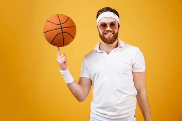Deportista sonriente en gafas de sol con baloncesto en el dedo