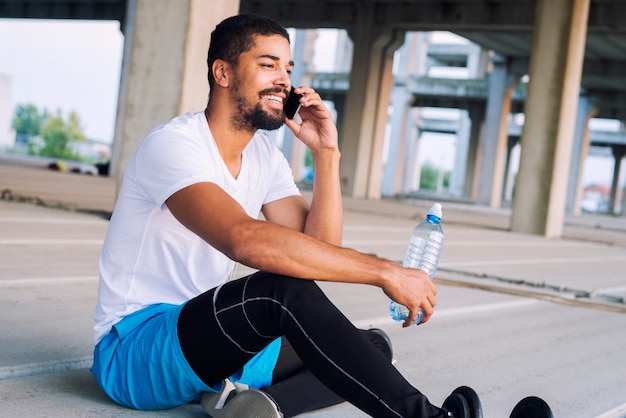 Deportista sonriente terminó de entrenar en el gimnasio, descansando, mediante teléfono móvil