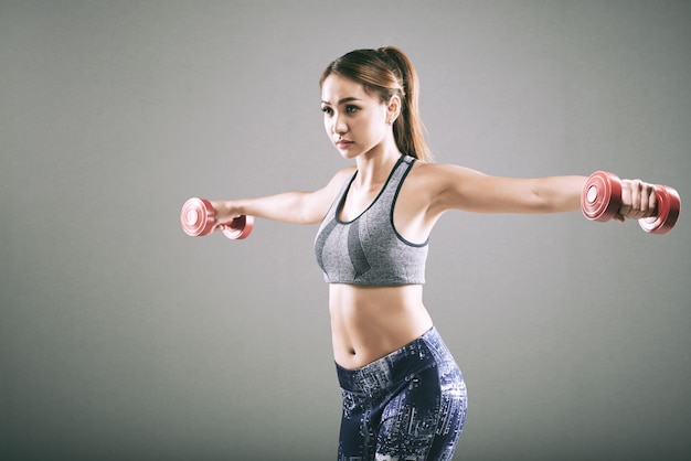 Deportiva chica asiática haciendo elevación lateral con pesas