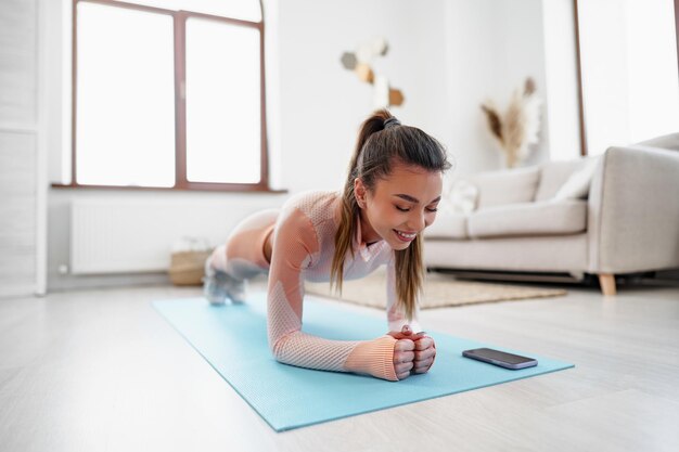 Deportiva joven haciendo ejercicio de tabla en el interior de casa