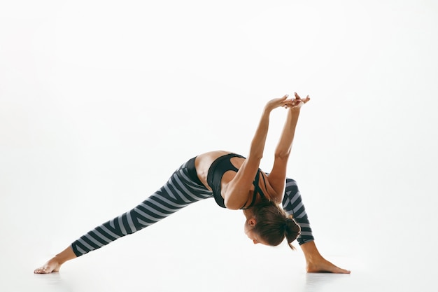 Deportiva joven haciendo práctica de yoga aislada en el espacio en blanco. Colocar modelo femenino flexible practicando