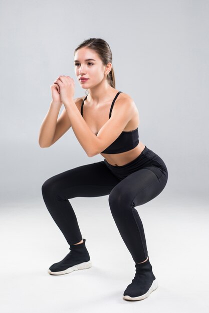 Deportiva mujer atlética en cuclillas haciendo abdominales en el gimnasio aislado sobre la pared blanca