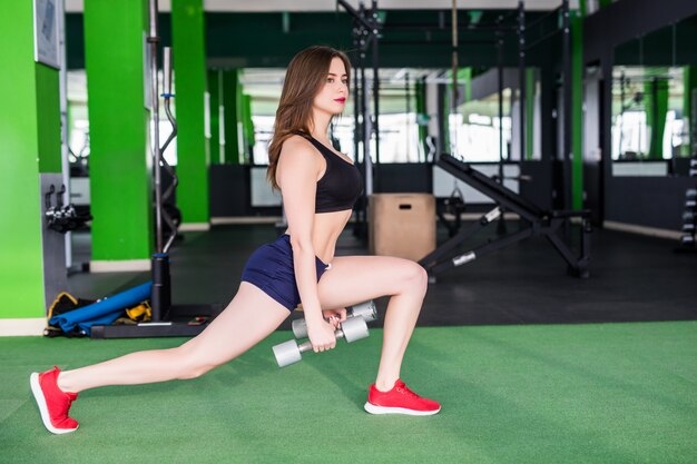 Deportiva mujer con cuerpo en forma fuerte está haciendo diferentes ejercicios en el moderno club deportivo con espejos