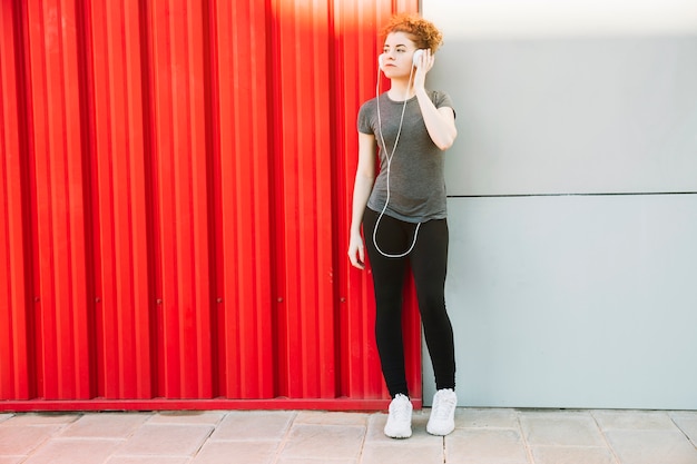 Deportiva mujer disfrutando de la música junto a la pared roja