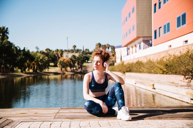 Deportiva mujer escuchando música en el muelle