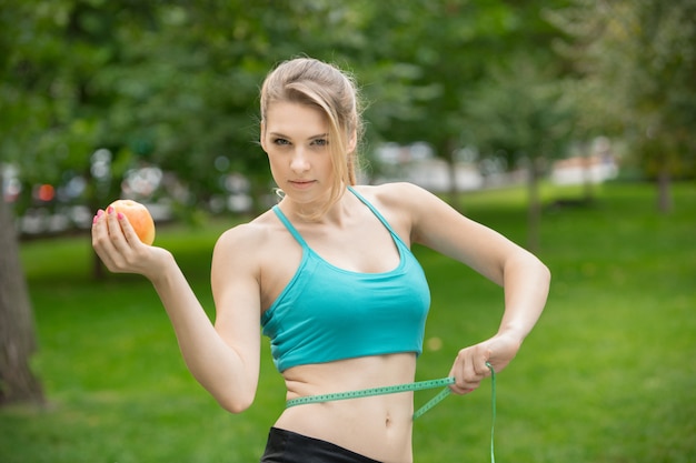 Deportiva mujer joven con manzana y cinta métrica