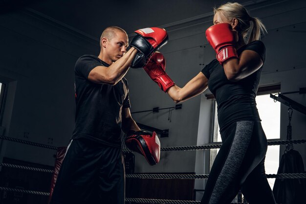 Deportiva mujer rubia tiene entrenamiento de boxeo con su entrenador experimentado.