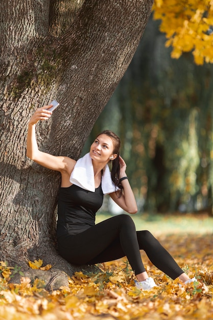 Deportiva mujer tomando selfies cerca de un árbol