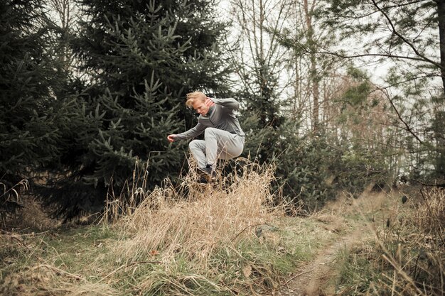 Deportivo joven saltando por encima de la hierba en el bosque