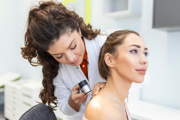 Dermatólogo en guantes de látex sosteniendo dermatoscopio mientras examina a un paciente atractivo con enfermedad de la piel Dermatóloga examinando a un paciente con dermascopio en busca de signos de cáncer de piel