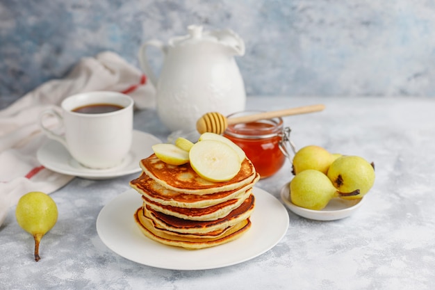 Desayuno casero: tortitas de estilo americano servidas con peras y miel con una taza de té en concreto. Vista superior y copia