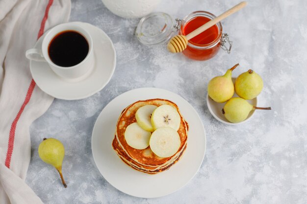 Desayuno casero: tortitas de estilo americano servidas con peras y miel con una taza de té en concreto. Vista superior y copia