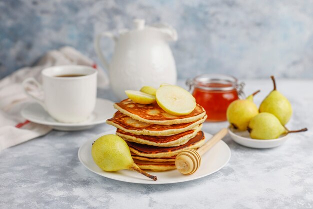 Desayuno casero: tortitas de estilo americano servidas con peras y miel con una taza de té en concreto. Vista superior y copia