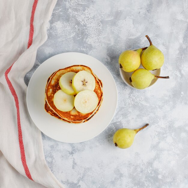 Desayuno casero: tortitas de estilo americano servidas con peras y miel con una taza de té en concreto. Vista superior y copia