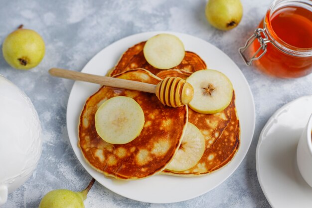 Desayuno casero: tortitas de estilo americano servidas con peras y miel con una taza de té en concreto. Vista superior y copia