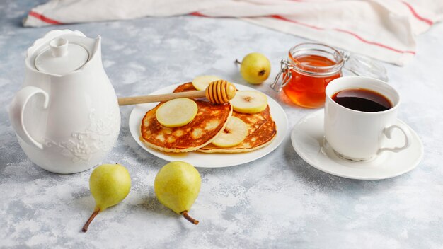 Desayuno casero: tortitas de estilo americano servidas con peras y miel con una taza de té en concreto. Vista superior y copia