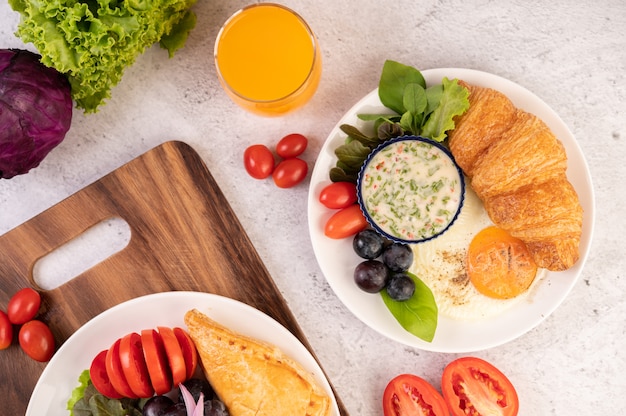 Foto gratuita el desayuno consiste en croissant, huevo frito, aderezo para ensalada, uvas negras y tomates.