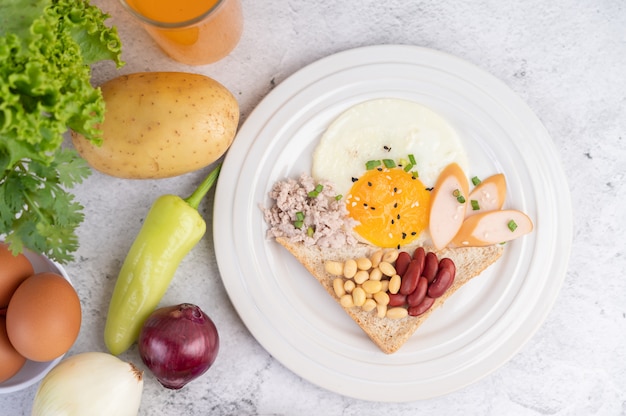 El desayuno consiste en huevos fritos, salchichas, carne de cerdo picada, pan, frijoles rojos y soja en un plato blanco.