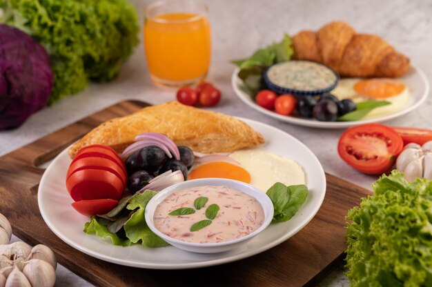 El desayuno consiste en pan, huevo frito, aderezo para ensalada, uvas negras, tomates y cebollas en rodajas.