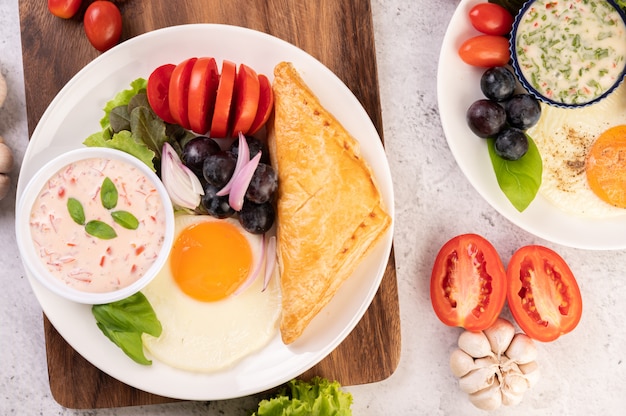 El desayuno consiste en pan, huevo frito, aderezo para ensalada, uvas negras, tomates y cebollas en rodajas.