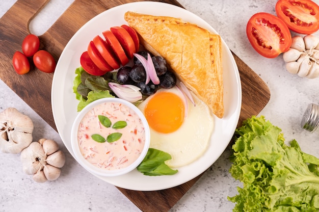El desayuno consiste en pan, huevo frito, aderezo para ensalada, uvas negras, tomates y cebollas en rodajas.