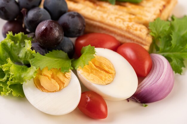 El desayuno consiste en pan, huevos duros, aderezo de ensalada de uva negra, tomates y cebollas en rodajas.