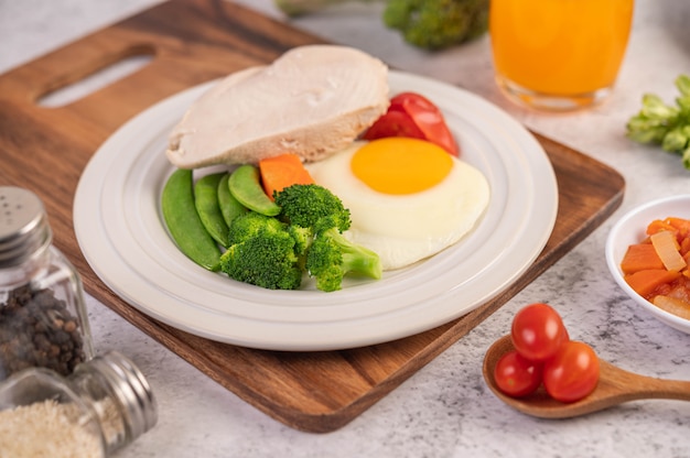 El desayuno consiste en pollo, huevos fritos, brócoli, zanahorias, tomates y lechuga en un plato blanco.