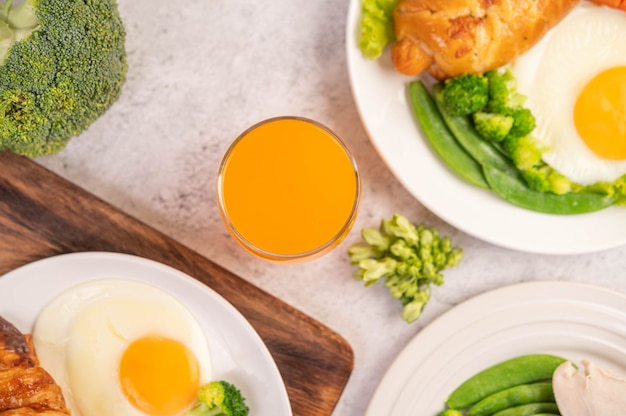 El desayuno consiste en pollo, huevos fritos, brócoli, zanahorias, tomates y lechuga en un plato blanco.