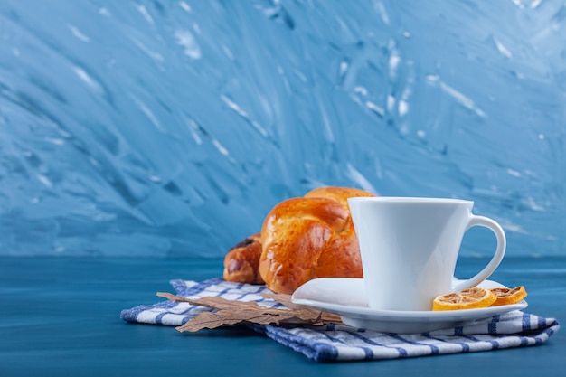 Desayuno continental con cruasanes recién hechos, una taza de té y limones en rodajas sobre un paño de cocina.
