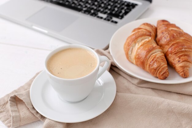 Desayuno con croissants y café cerca de una computadora portátil.