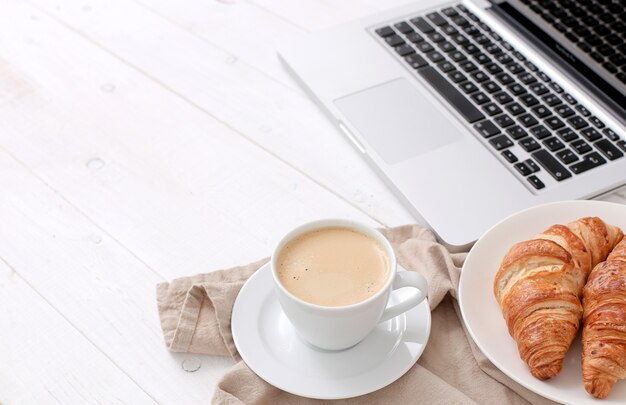 Desayuno con croissants y café cerca de una computadora portátil.