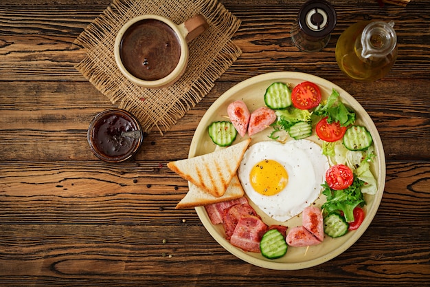 Desayuno en el Día de San Valentín: huevo frito en forma de corazón, tostadas, salchichas, tocino y verduras frescas. Desayuno inglés. Taza de cafe. Vista superior