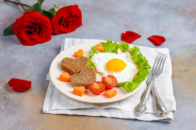 Desayuno el día de San Valentín: huevos fritos y pan en forma de corazón y verduras frescas.