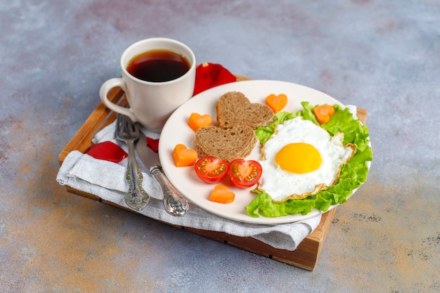 Desayuno el día de San Valentín: huevos fritos y pan en forma de corazón y verduras frescas.