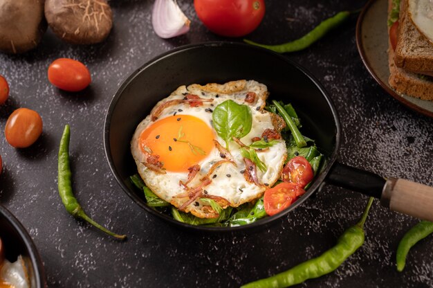 Desayuno con huevos fritos, salchicha y jamón en una sartén con tomates. Chile y albahaca