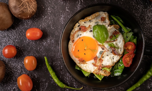 Desayuno con huevos fritos, salchicha y jamón en una sartén con tomates. Chile y albahaca