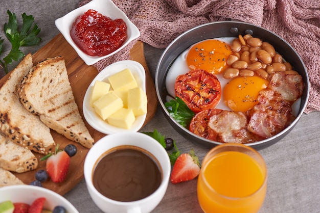 Desayuno inglés en sartén con huevos fritos, tocino, frijoles, tomates asados.