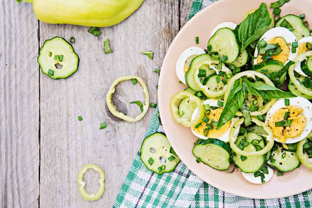 Desayuno en el jardín de verano. Ensalada de huevos y pepinos con cebolla verde y albahaca. Vista superior. Lay Flat