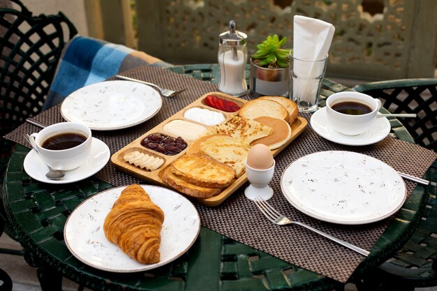 Desayuno con panqueques de crepes, tostadas, croissant, huevo, fresas en rodajas, plátanos y café.
