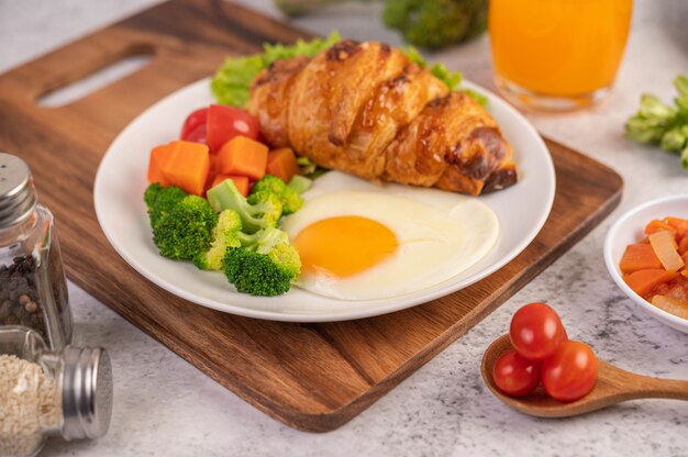 Desayuno que consiste en pan, huevos fritos, brócoli, zanahorias, tomates y lechuga en un plato blanco.