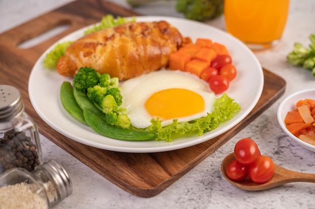 Desayuno que consiste en pan, huevos fritos, brócoli, zanahorias, tomates y lechuga en un plato blanco.