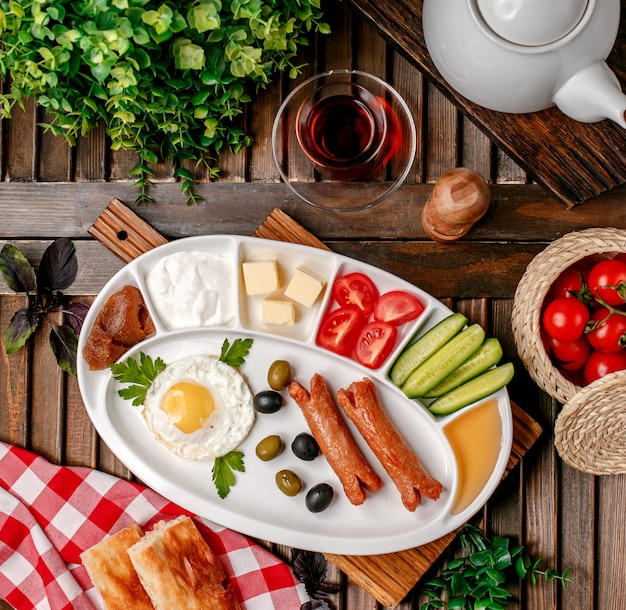 Desayuno con salchichas fritas, huevos y verduras.