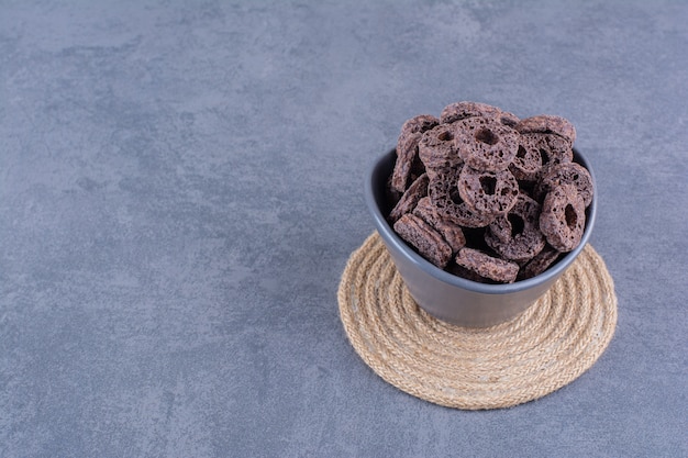 Desayuno saludable con anillos de maíz de chocolate en un cuenco negro sobre piedra.