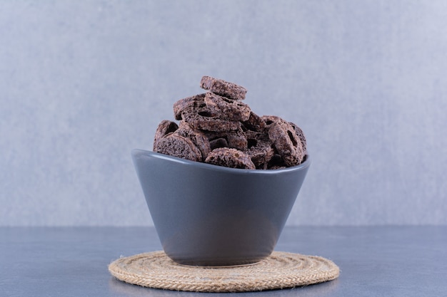 Desayuno saludable con anillos de maíz de chocolate en un recipiente negro sobre una piedra.