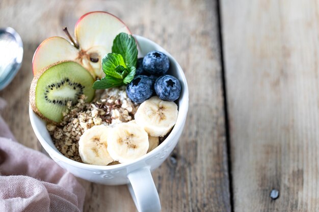 Desayuno saludable avena o granola con arándanos, manzana, kiwi y menta sobre un fondo rústico de madera, primer plano, espacio para copiar