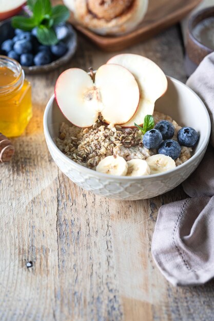 Desayuno saludable avena o granola con arándanos, manzana y miel sobre un fondo rústico de madera. Copiar espacio.