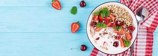 Desayuno saludable - granola, fresas, cerezas, nueces y yogurt en un recipiente sobre una mesa de madera. Concepto de comida vegetariana. Vista superior